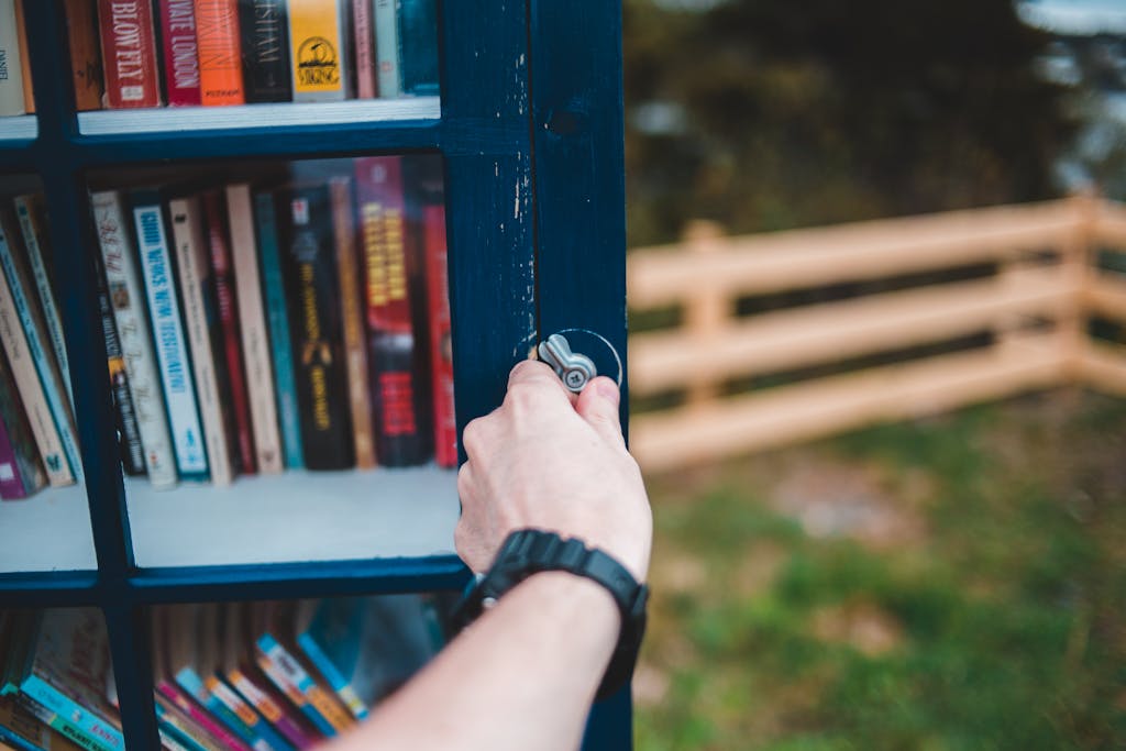 A person opening a little free library filled with books in a park setting.